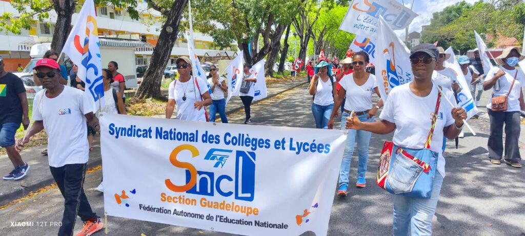 Le SNCL en manifestation, ici en Guadeloupe. Une foule de manifestants défile derrière une banderole du SNCL.